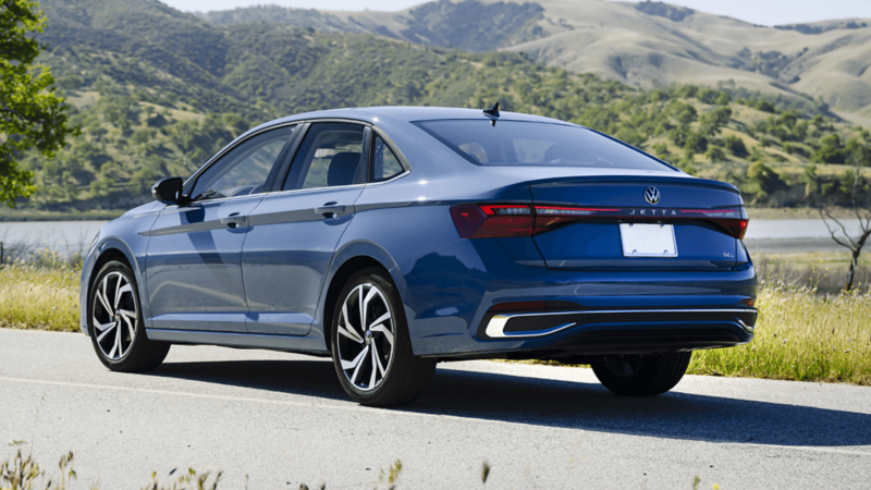 Vue arrière latérale de la Volkswagen Jetta 2026 bleue, stationnée au bord d’une route avec vue sur les collines.