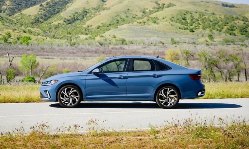 Profile view of a Jetta shown in Monterey Blue Pearl parked with wooded hills in the background.