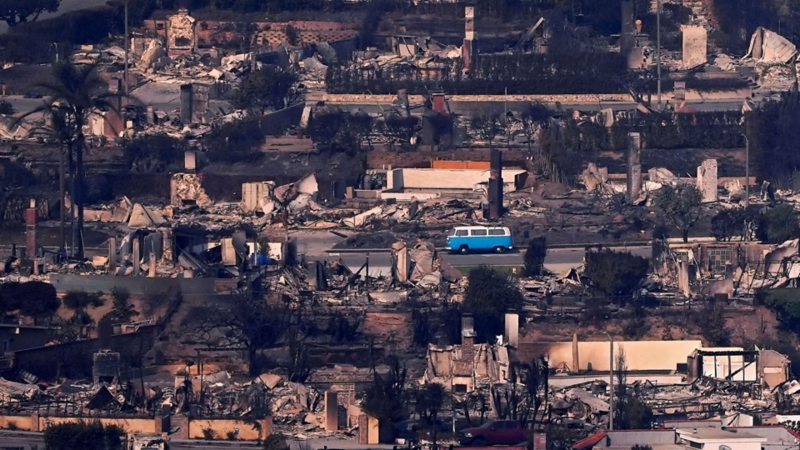 A retro blue Volkswagen bus parked on a street among a burned cityscape destroyed by wildfire