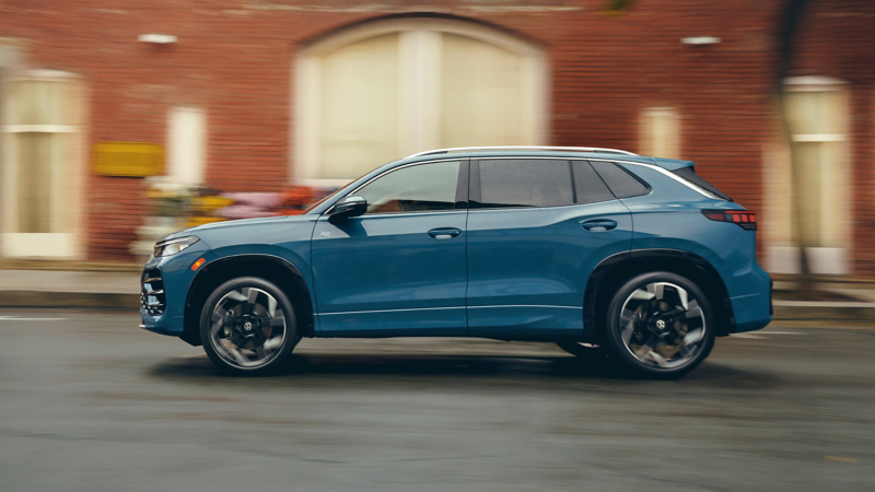 Perfil lateral de un Tiguan mostrado en Monterey Blue Pearl con un edificio de ladrillo al fondo.