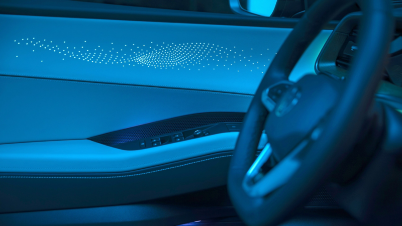 View from the front passenger seat looking at the available interior ambient lighting design in the front drivers door with the steering wheel soft focused in frame and a soft glow illuminating the interior. 