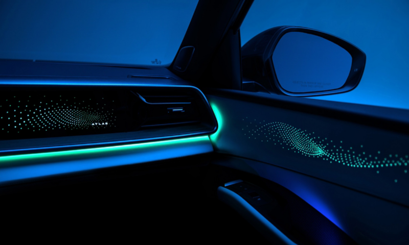 Detail view of the available interior ambient lighting casting a warm glow on the front passenger door and dash with a dramatically lit studio setting visible through the windshield.