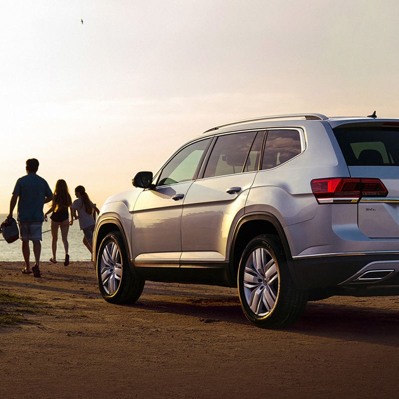 Volkswagen Atlas estacionado frente a la playa con un grupo de personas que camina hacia la playa. 