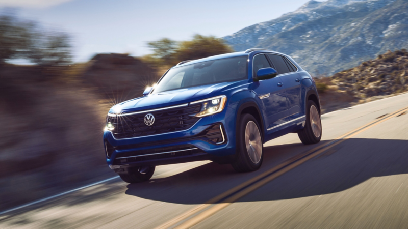 A front view of an Atlas Cross Sport shown in Mountain Lake Blue driving on a wooded mountain road.