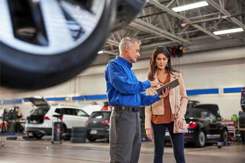 En el interior del garaje de un centro de servicio, un cliente interesado habla con un especialista en ventas/productos de Volkswagen en un concesionario.