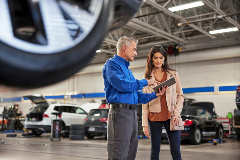 A man showing a woman a document in the middle of an auto repair shop.