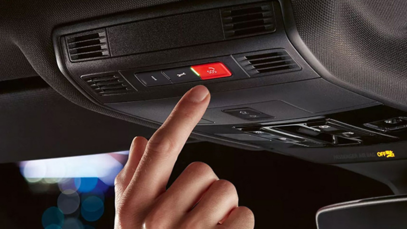 Close-up of a hand pressing red button on interior roof of vehicle.