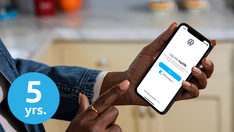 A close-up on a smartphone a woman is holding. On the screen we can see she’s logging into the myVW app to use the remote vehicle features. In the lower left corner of the image is a light blue circular icon with a numeral and text reading “5 years.”