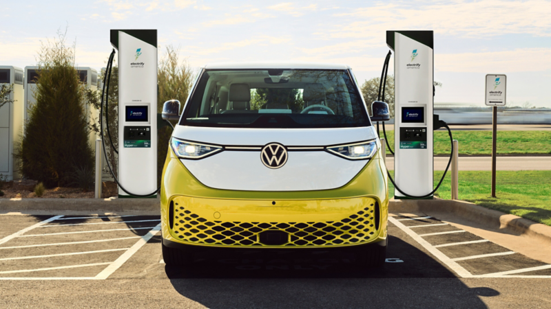 Head-on view of an ID. Buzz shown in Pomelo Yellow Metallic and Candy White parked at an electric vehicle charging station.