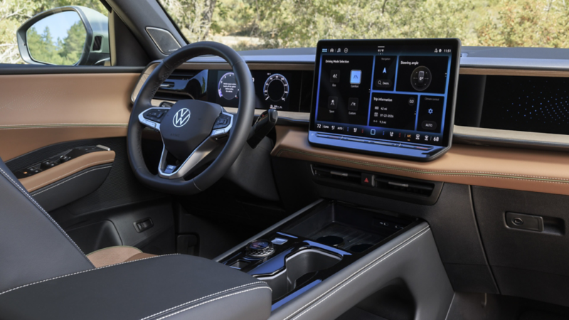 Interior view of an Atlas Cross Sport showing the steering wheel, VW Digital Cockpit and available 15" center touchscreen display while trees are visible through the window and windshield.