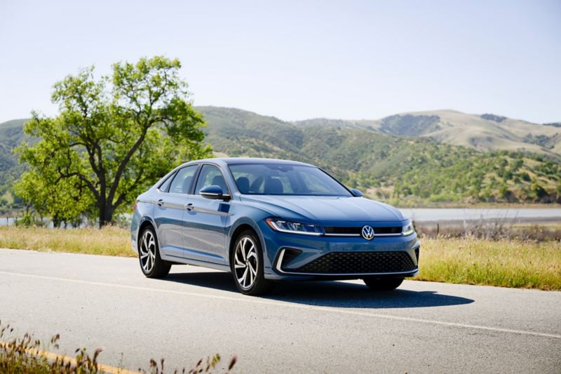 Vista frontal de un Jetta en Monterey Blue Pearl estacionado con colinas boscosas en el fondo.