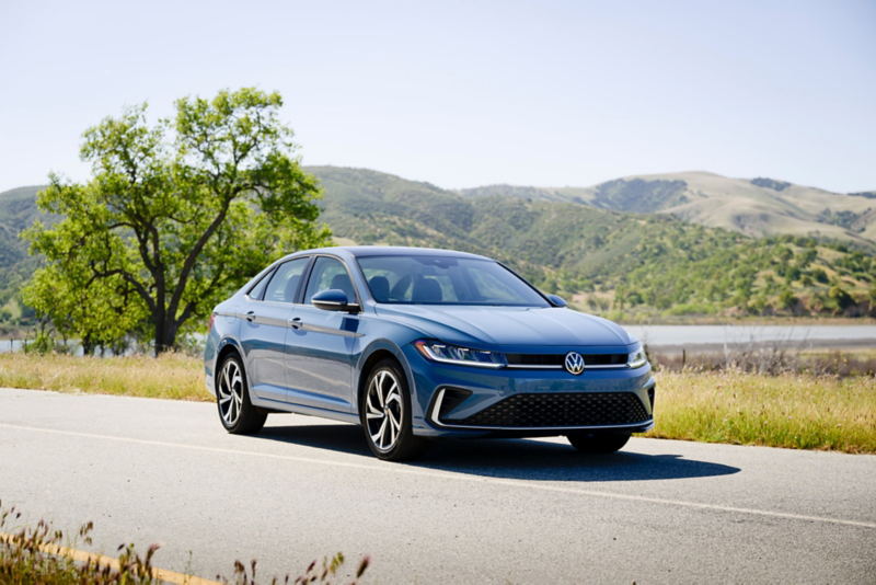 Front view of a Jetta shown in Monterey   Blue Pearl parked with wooded hills in the background.