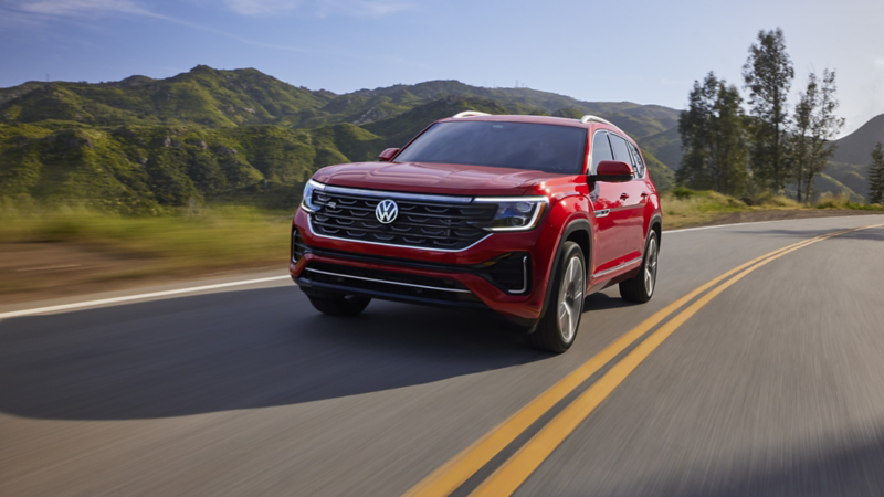 Atlas shown in Aurora Red Metallic seen from the front as it drives on a wooded mountain road.