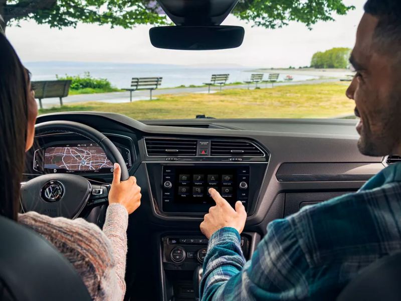 Una pareja joven ve el pintoresco lago a través del parabrisas de su Volkswagen Tiguan, con una impresionante tecnología interior.