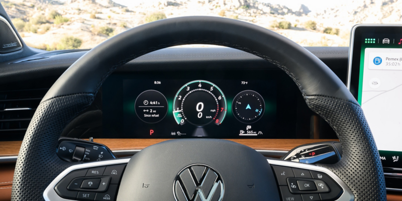 Close up view of the VW Digital Cockpit Pro and available heated steering wheel in a Tiguan with rocky mountains visible through the windshield.