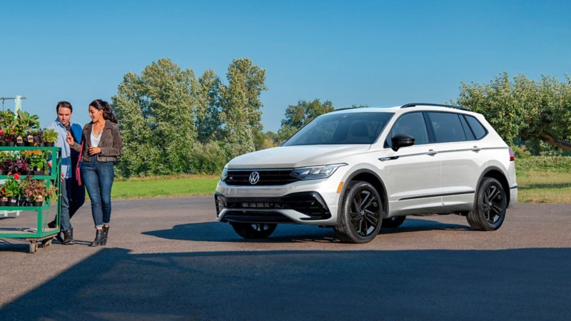 Two people standing nearby the 2023 VW Tiguan, shown in Opal White from front three-quarters view. 