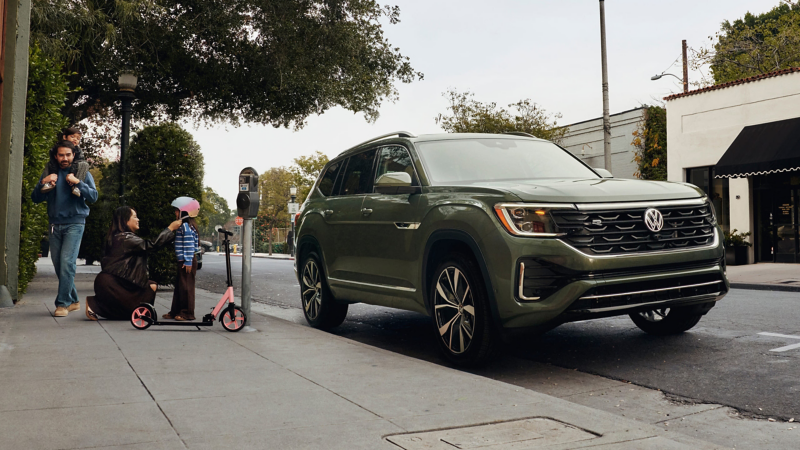 An Atlas shown in Avocado Green Metallic is parked on an urban street while a family next to the vehicles prepares for an afternoon outing.