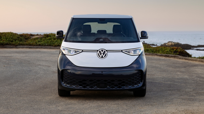 Front view of an ID. Buzz shown in Blue Charcoal Metallic and Candy White parked on a brush lined road with the ocean in the background.