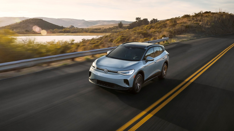 Front view of an ID.4 shown in Arctic Blue Metallic driving with mountains and a lake in the background.