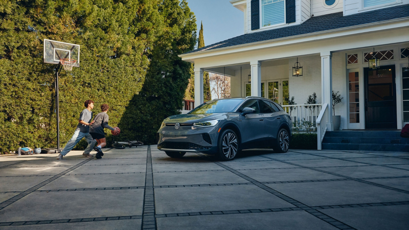 An ID.4 electric vehicle shown in Pure Gray is parked in the driveway of a stately home while two children play basketball nearby.
