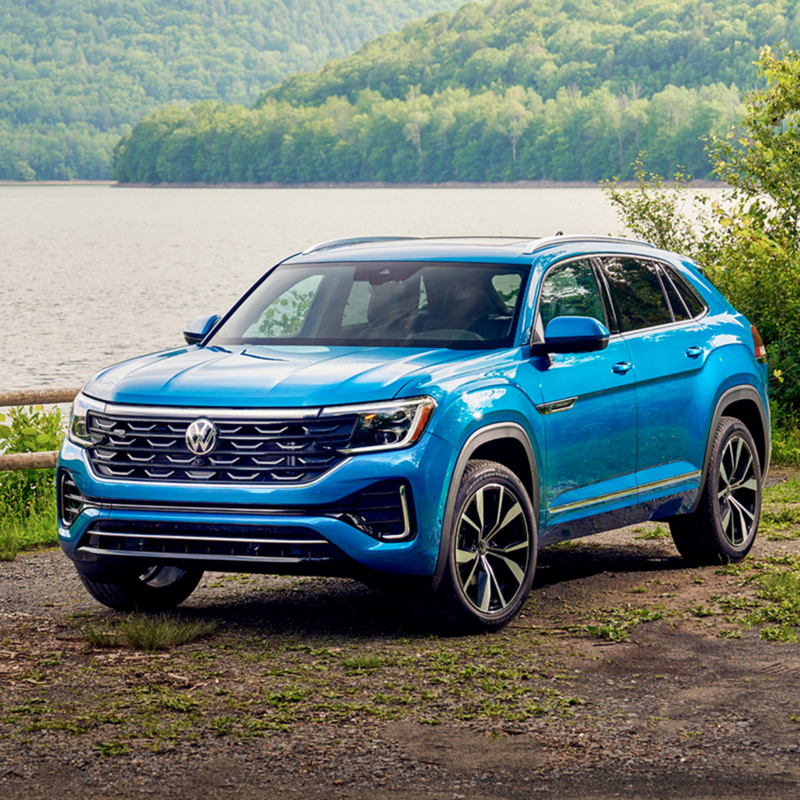 Atlas Cross Sport shown in Kingfisher Blue Metallic parked in front of a lake with a forest in the background.