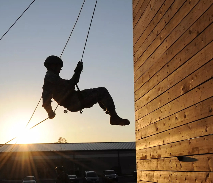 A soldier rappels down a wooden wall at sunrise.