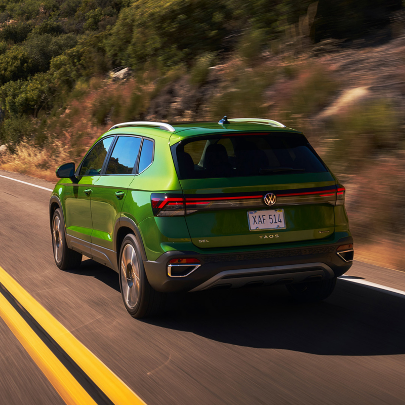 Rear view of a Taos shown in Bright Moss Green driving on a mountain road.