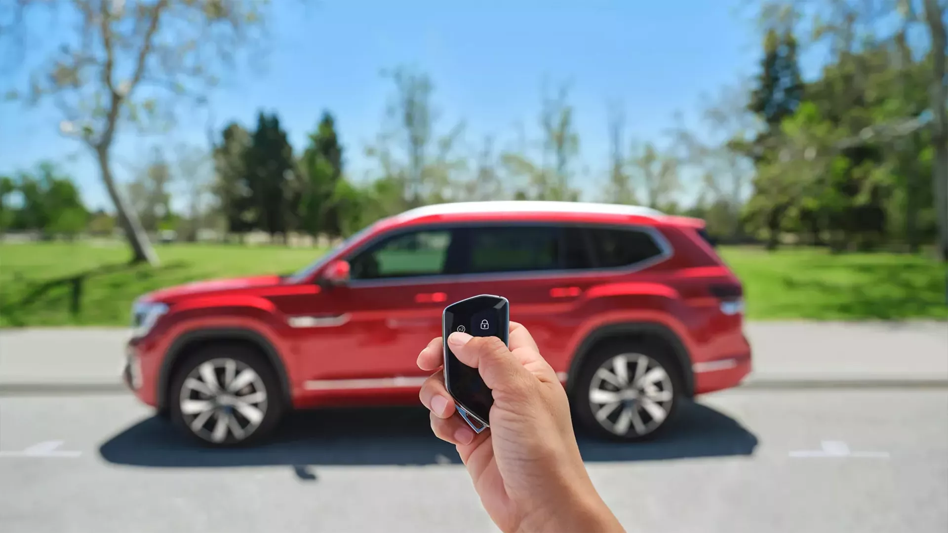 first person point of view of wireless keyphob held in front of a New 2024 Red Volkswagen Atlas 6 seat SUV in the foreground