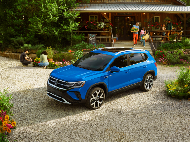 A couple walks down the steps of garden center with flowers, a Cornflower Blue Taos parked along gravel.