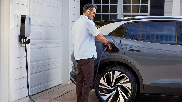 A man plugs in a charger into a Gray ID.4 in front of a modern home in the driveway.