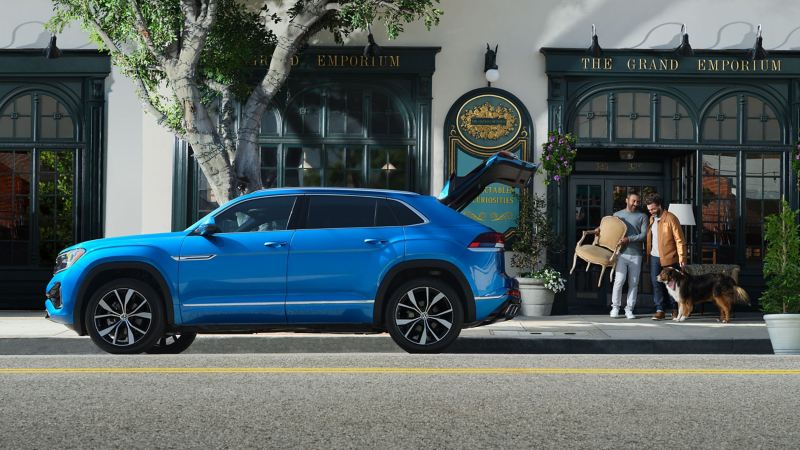 Young couple and dog leave antique furniture shop with a chair to load in kingfisher blue metallic VW Atlas Cross Sport.