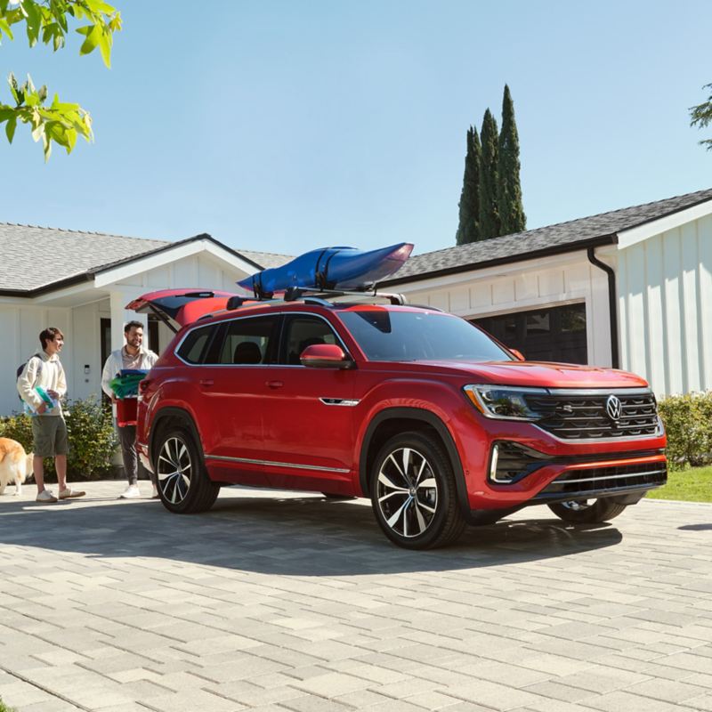 A family of four load up the trunk of their kayak-topped VW Atlas in Aurora Red Metallic in their house driveway.