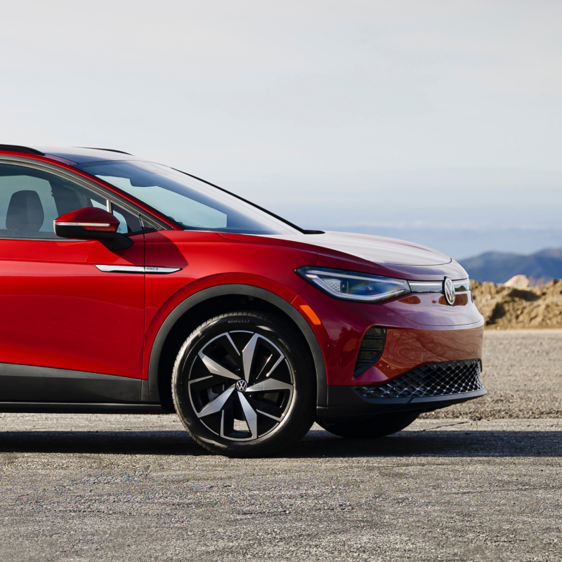 An ID.4 shown in Aurora Red Metallic parked on road with mountains in the background.