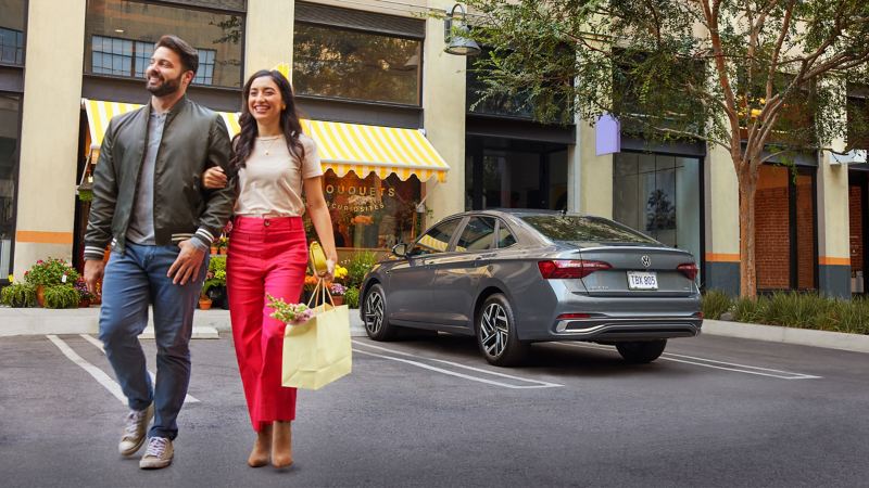 Happy young woman shows a successful trip to the florist as she passes a parked platinum gray metallic VW Jetta SEL.