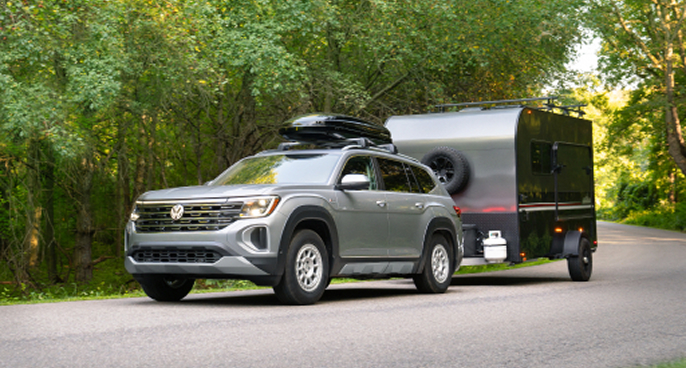 A 2025 Atlas in Silver Mist Metallic with a optional accessory cargo carrier on the roof and optional accessory Traverse MX wheels pulling a camping trailer