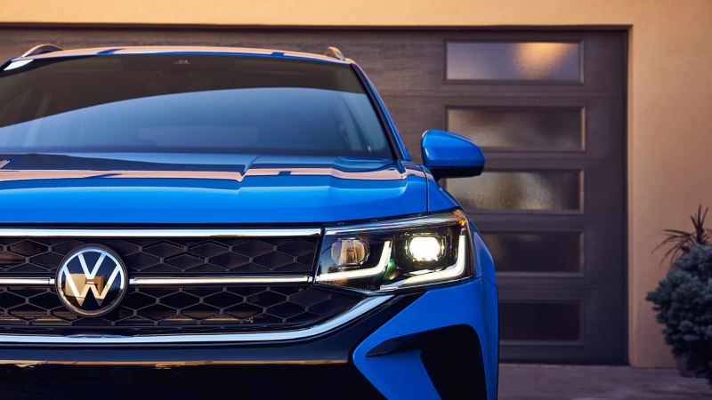 Zoomed in front view of a VW Taos in Cornflower Blue parked in front of contemporary-style garage.