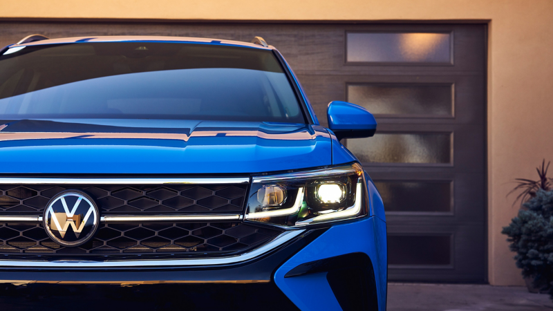 Zoomed in front view of a VW Taos in Cornflower Blue parked in front of contemporary-style garage.