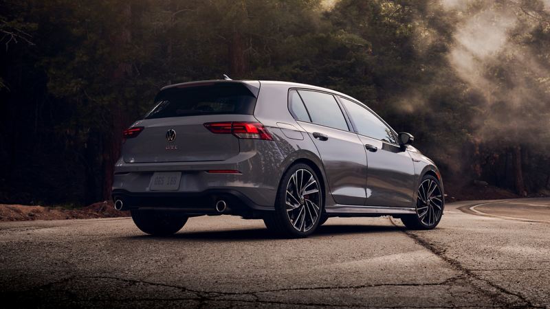 A parked VW Golf GTI in Moonstone Gray showing the angled silhouette on a foggy winding woodland backroad.