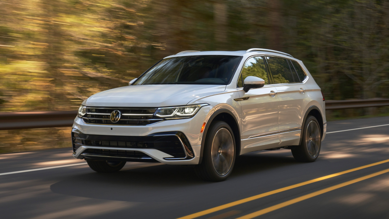 Sunrise shines and bursts through slender trees as a VW Tiguan in Opal White curves around open woodland road.