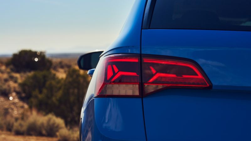 Zoomed in taillight of VW Taos in Cornflower Blue with blurred verdant landscape and open skies.