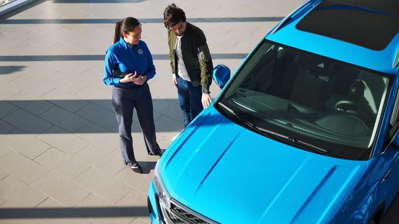A man and a woman stand next to a Taos in Cornflower Blue at a Volkswagen dealership.