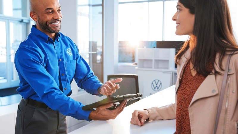 Un hombre y una mujer se sonríen en un mostrador de servicio en un concesionario Volkswagen.