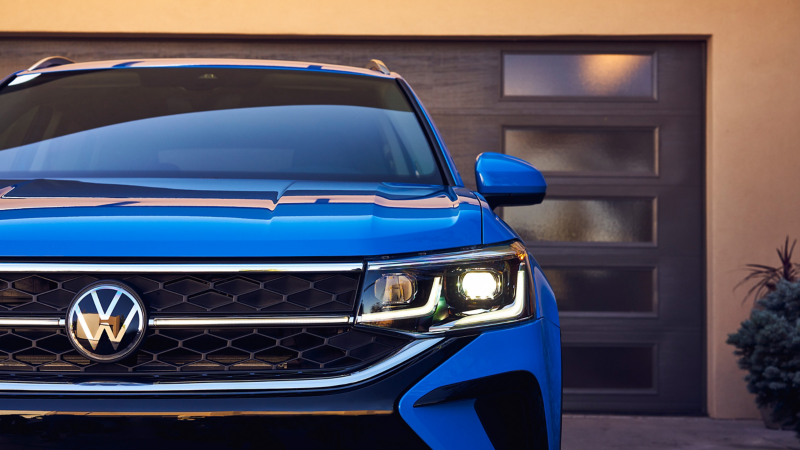 A Volkswagen Taos in Cornflower Blue in front of a modern garage.