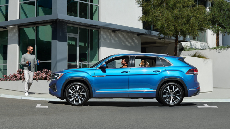 Side profile of a parked Atlas Cross Sport in Kingfisher Blue Metallic as a man walks up with coffee.