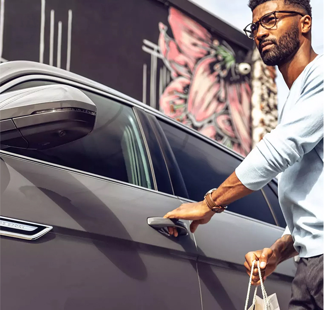 A bearded man with glasses is opening the driver door to his Volkswagen.