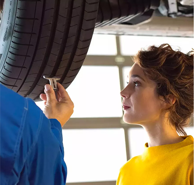 A young woman in a mustard yellow sweater is being shown the status of her VW's tire by a technician.