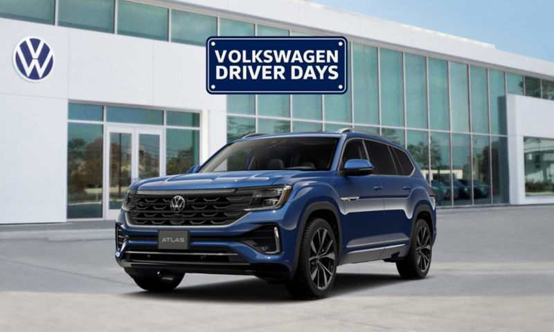 Front view of a Atlas shown in Mountain Lake Blue parked in front of a VW dealership with a Volkswagen Driver Days graphic floating above the vehicle.