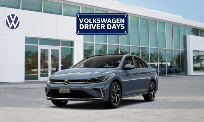 Front view of a Jetta shown in Monterey Blue Pearl parked in front of a VW dealership with a Volkswagen Driver Days graphic floating above the vehicle.