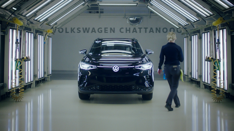 Frontal view of an ID.4 displayed on the factory floor of VW's Chattanooga facility, with an engineer standing beside it.