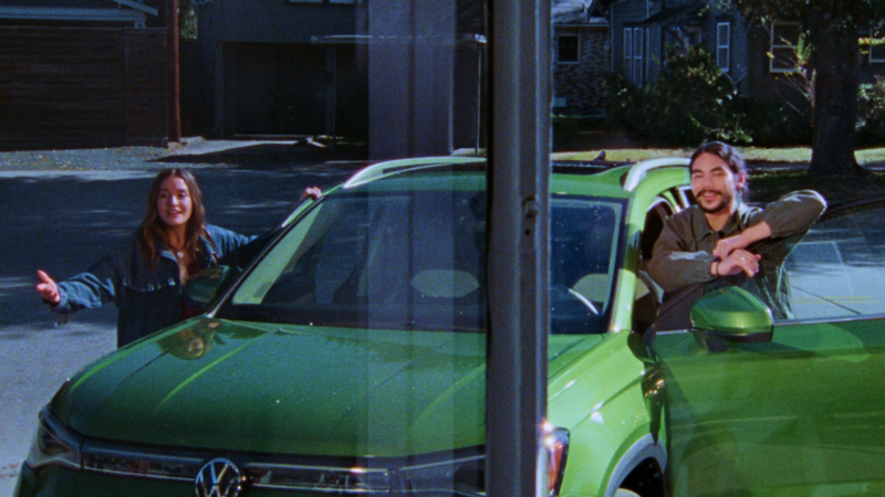 Two people standing next to a Taos shown in Bright Moss Green looking in the direction of the camera in a residential neighborhood.